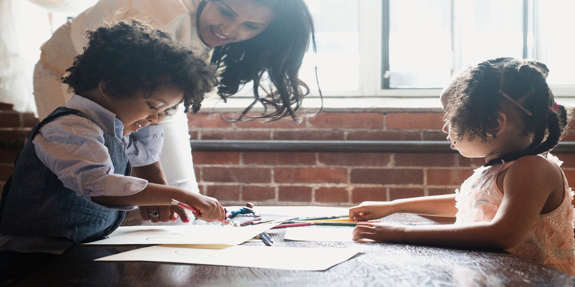 A mother and her children sitting at a table, happily coloring together with crayons and paper.